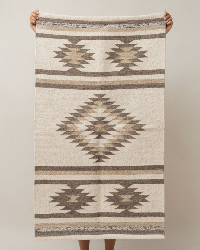 Person holding a patterned rug with geometric design on a plain background