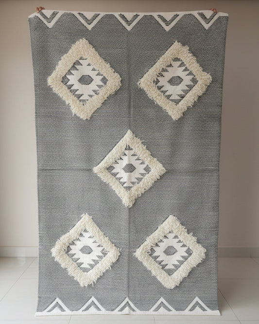 Gray and white patterned rug displayed in a store setting with fabric shelves in the background.