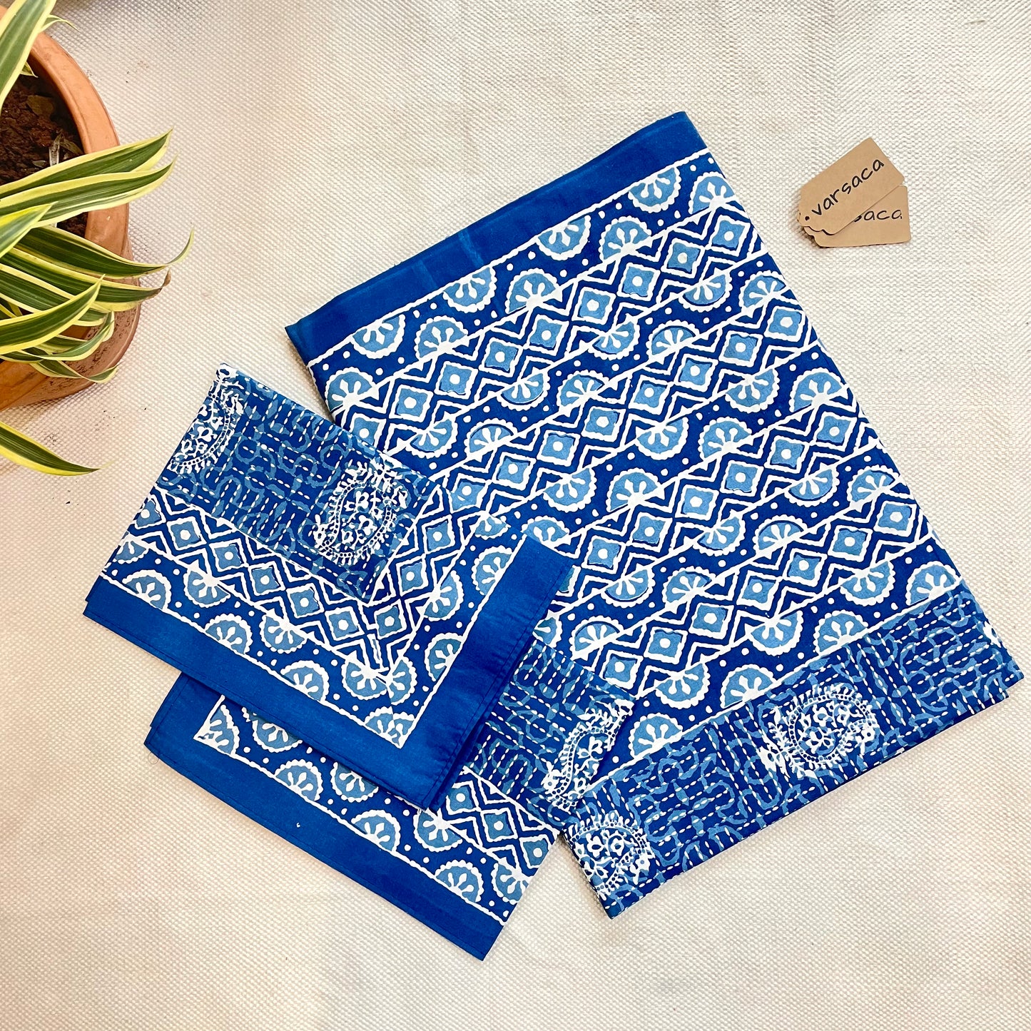 Folded indigo blue batik print king-size bedsheet with a plain border and geometric zigzag pattern on the border, displayed on a flat surface.