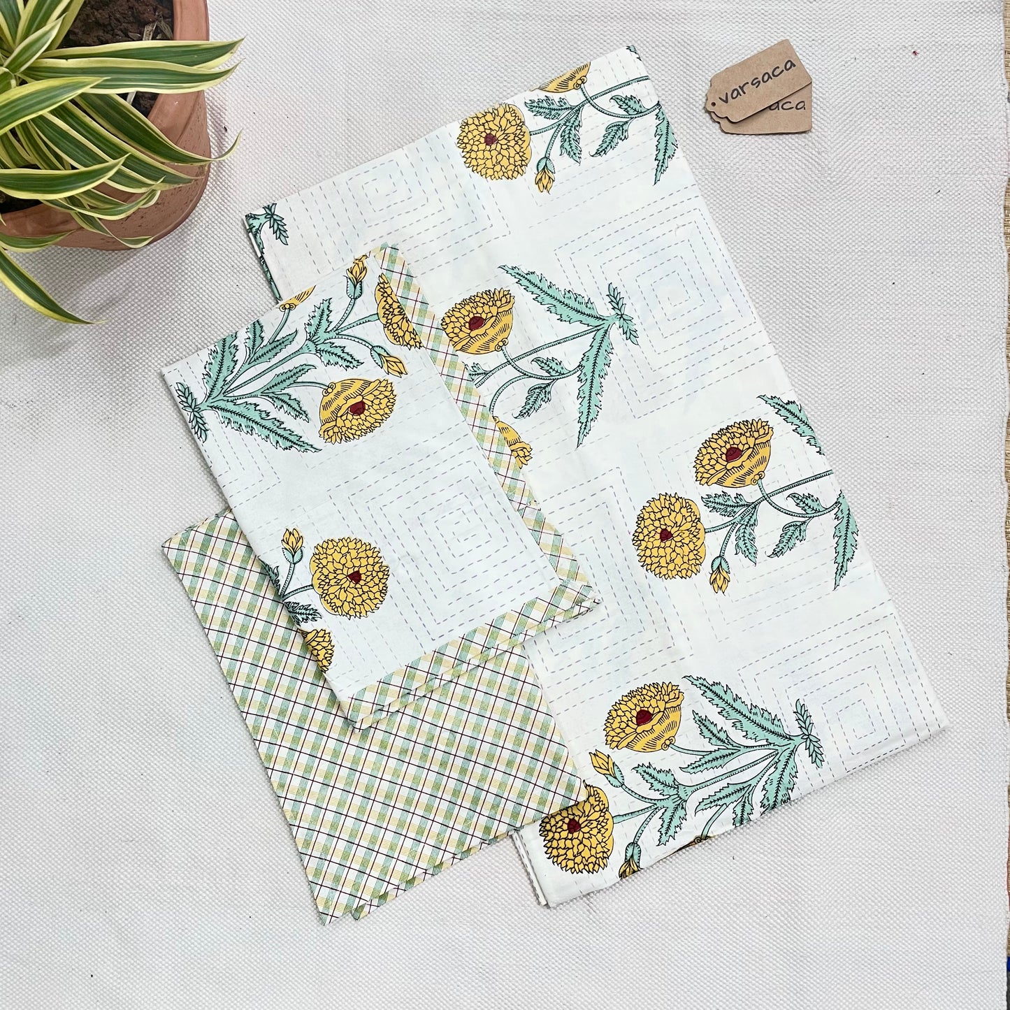 A king-size bedsheet with a yellow and white hand block print design, laid out flat with a part of the design showing a pineapple motif, placed on a white surface with a partial view of a green and white patterned fabric in the background.