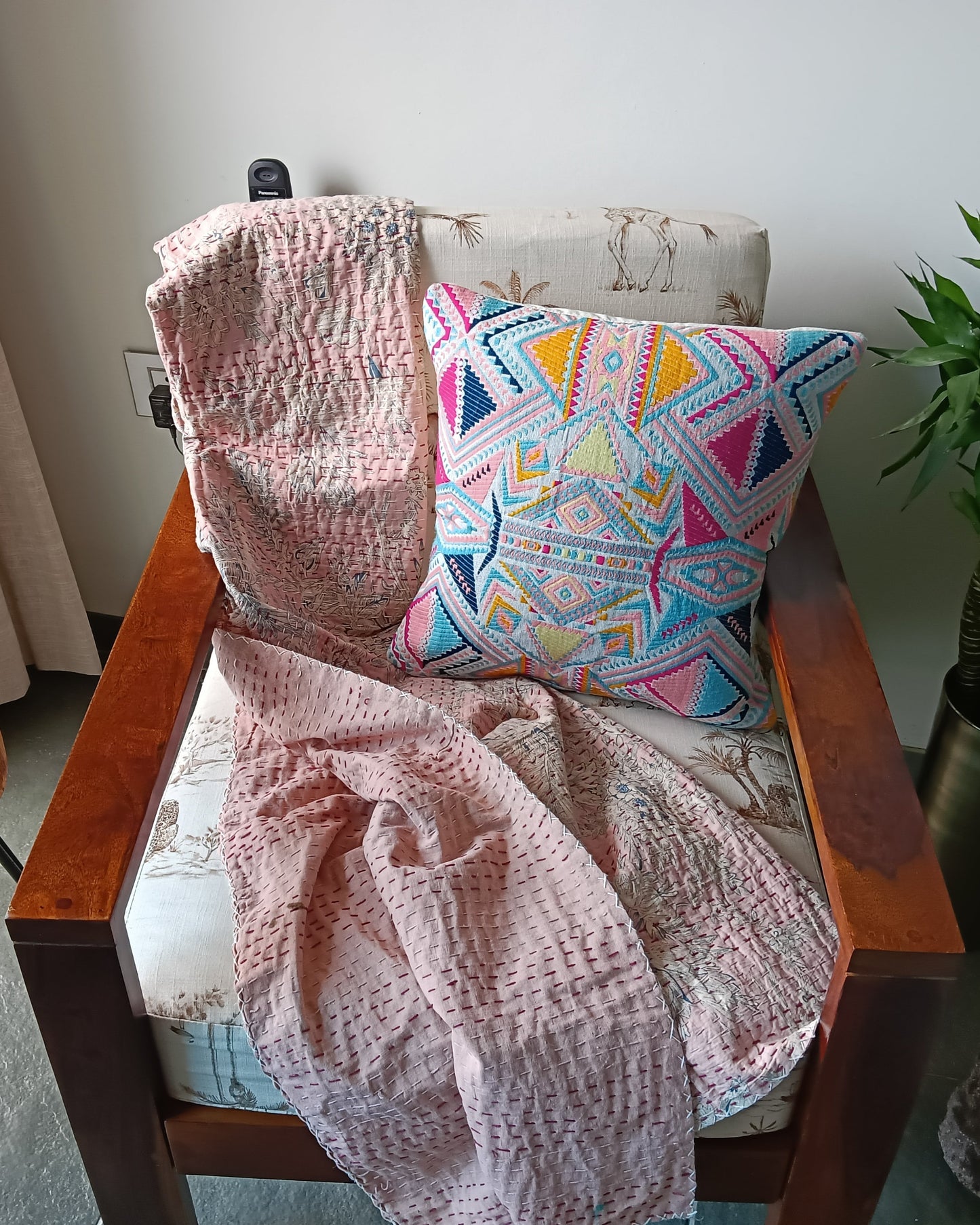 Chair with a pink blanket and colorful pillow, next to a wooden table with flowers and a plant.
