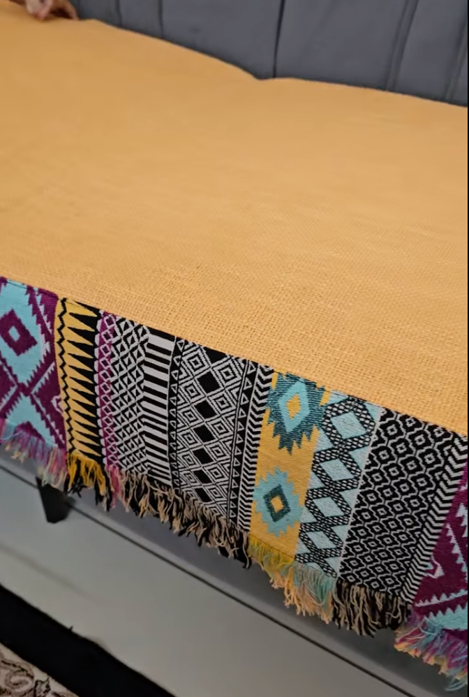 Colorful patterned blanket draped over a yellow surface with a gray background