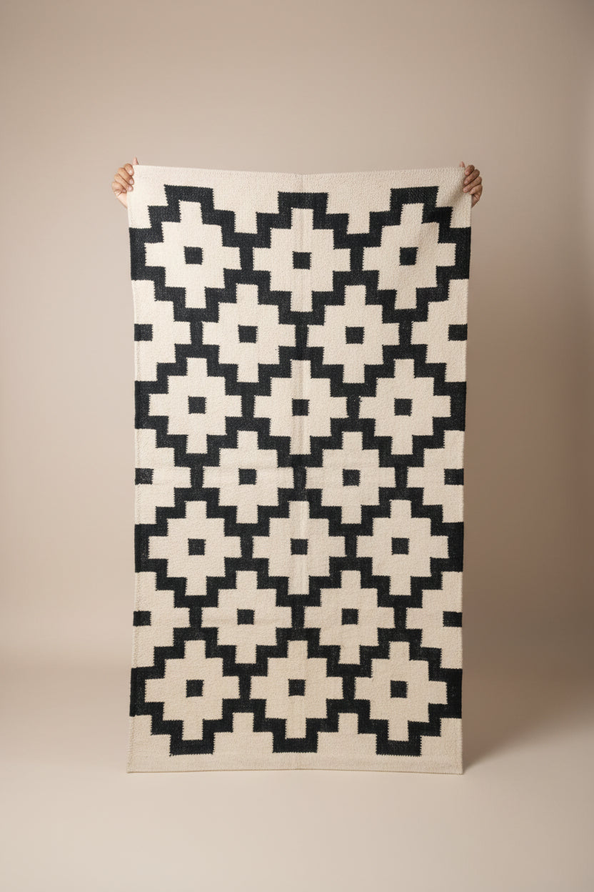 Person holding a geometric patterned rug in a room with shelves and various items.