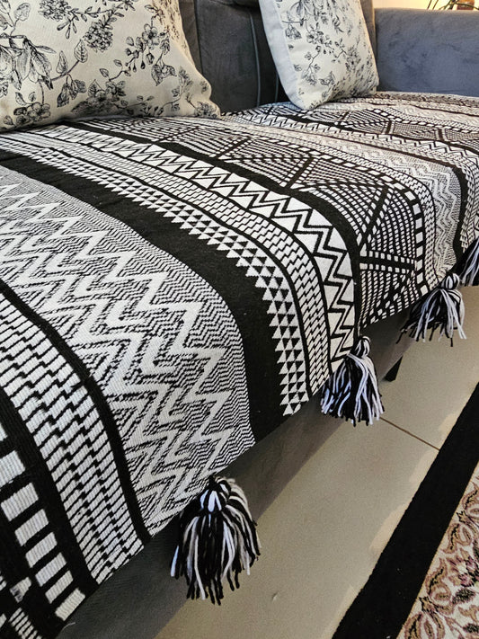 Black and white patterned throw blanket with tassels on a sofa.