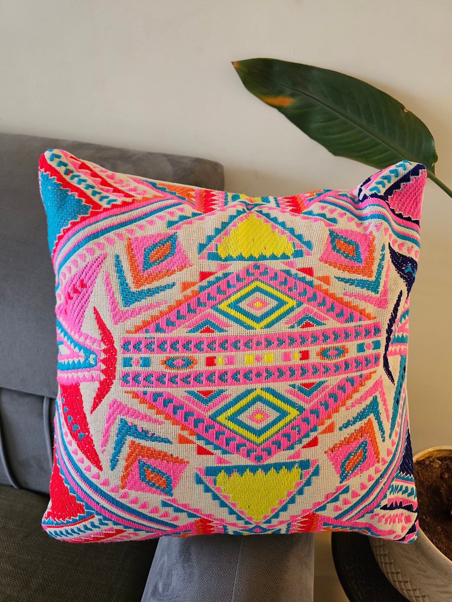 Colorful geometric patterned pillow on a gray surface with a plant leaf in the background