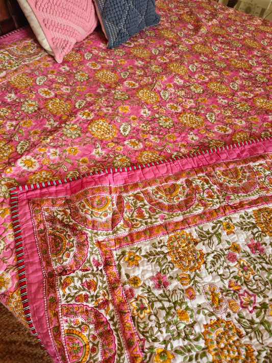 Colorful floral-patterned quilt on a bed with pink and blue pillows.