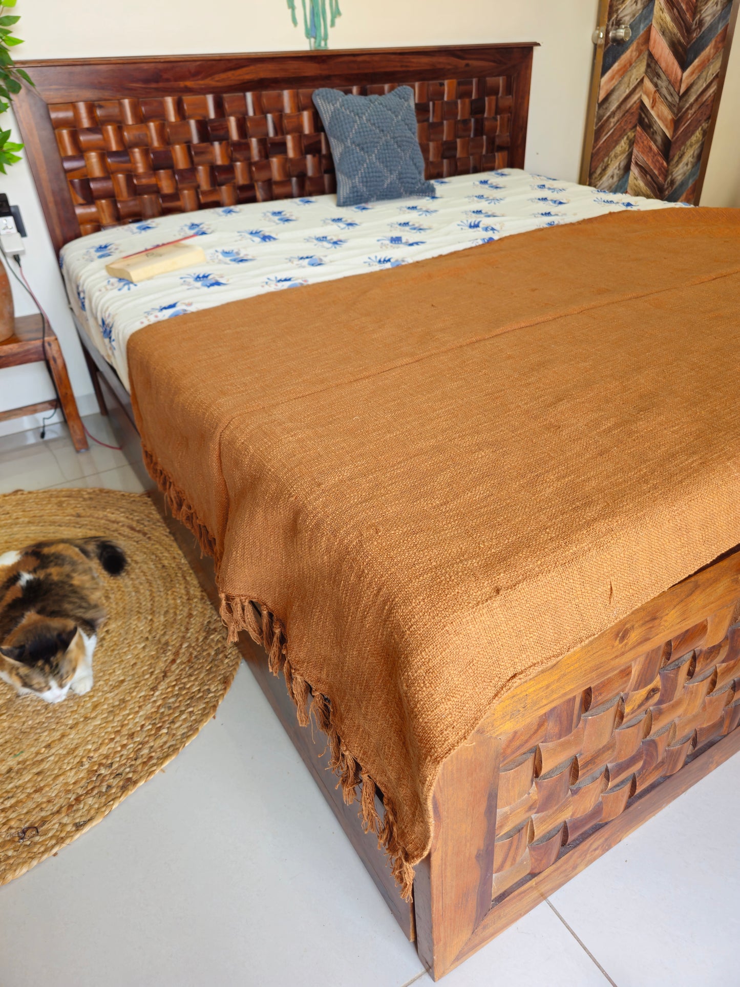 Wooden bed with brown blanket and woven headboard in a room setting.
