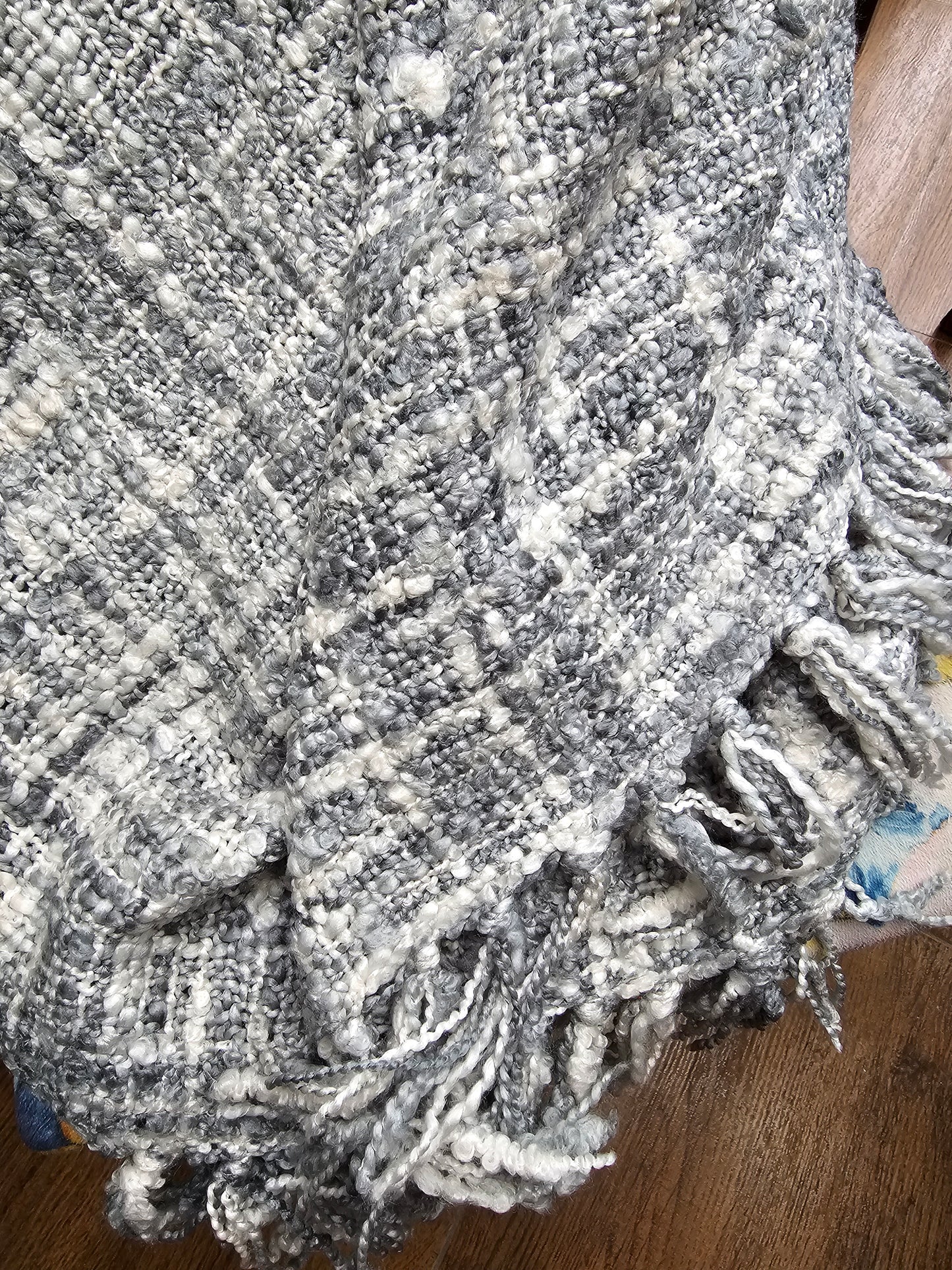Textured gray blanket with tassels on a wooden surface