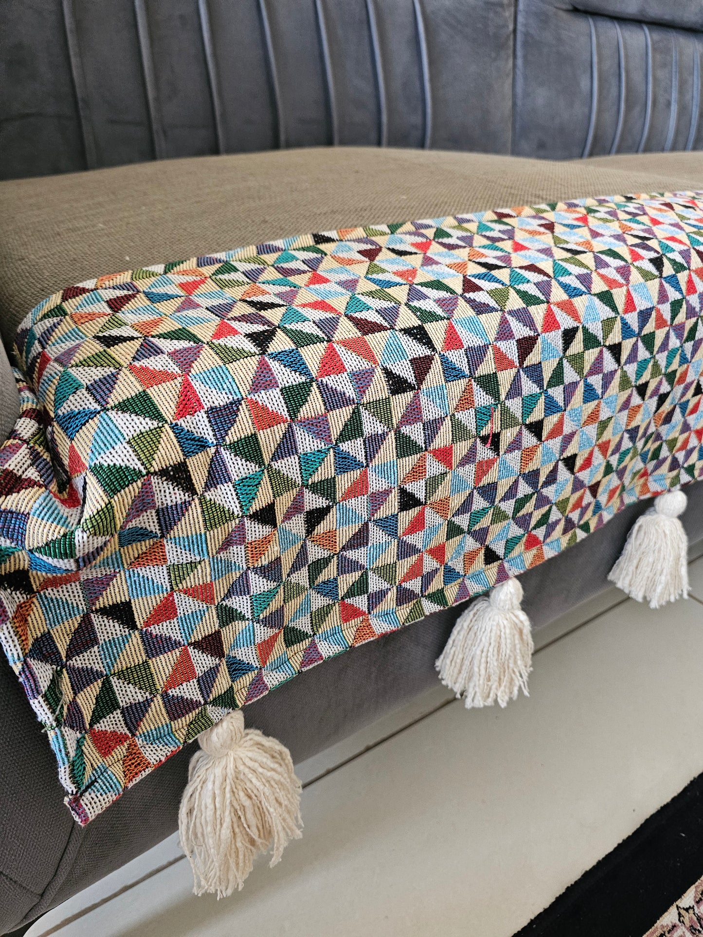 Multicolored geometric patterned throw blanket with tassels on a gray surface