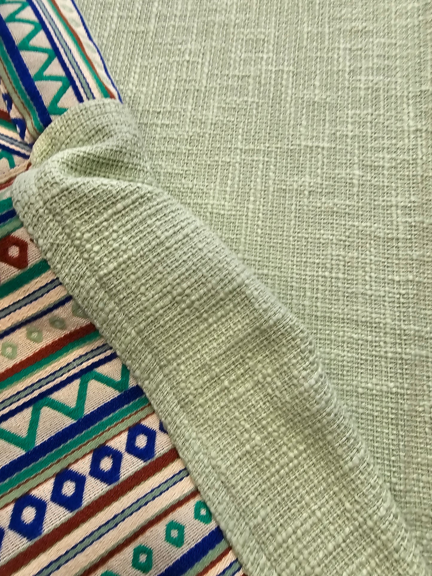 Close-up of a green textured fabric with a colorful patterned fabric underneath