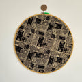 A round embroidery hoop with a geometric abstract pattern in shades of grey, framed with a wooden ring at the top.