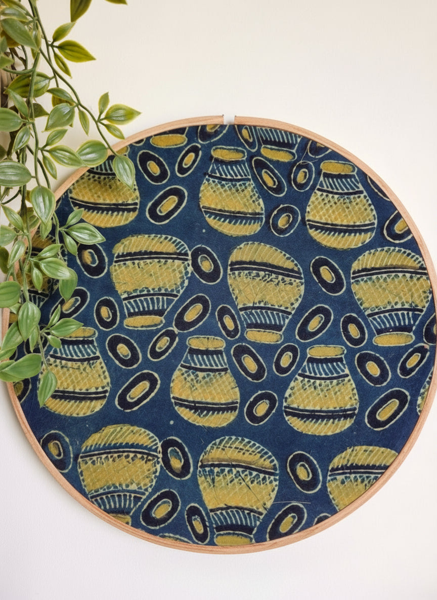 Embroidery hoop with blue fabric featuring yellow geometric patterns, against a white background.