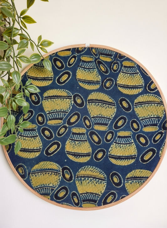 Embroidery hoop with blue fabric featuring yellow geometric patterns, against a white background.