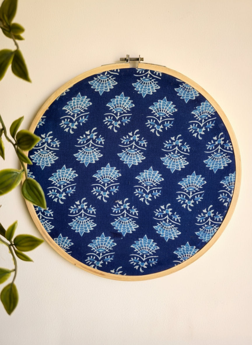 Embroidery hoop with blue and white floral pattern on a beige wall.