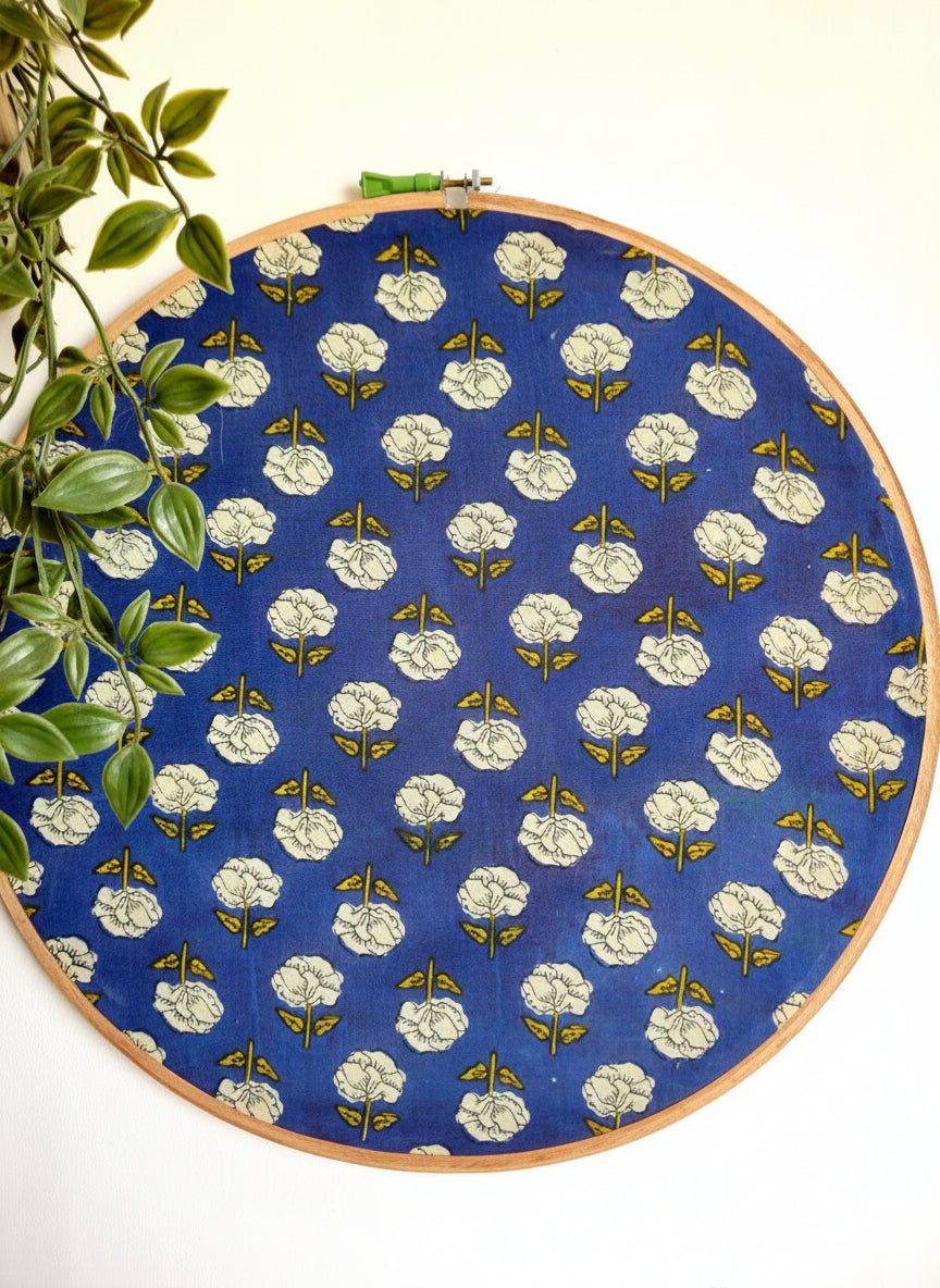 Embroidery hoop with blue fabric featuring white floral pattern, hanging against a white background.