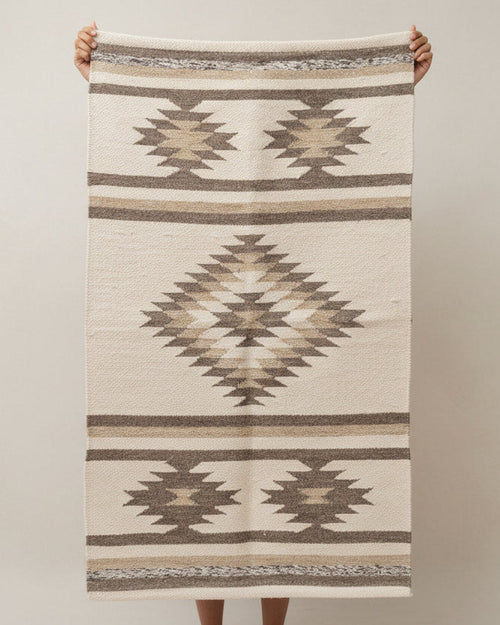 Person holding a patterned rug with geometric design on a plain background