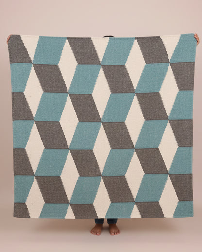 Person holding a geometric patterned blanket with blue and gray triangles on a plain background