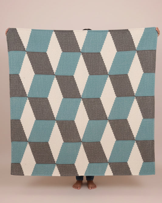Person holding a geometric patterned blanket with blue and gray triangles on a plain background