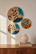 A round jute mat with hand-painted abstract leaves in vibrant colors and a sunflower design, featuring black leaves and a blue-green background.