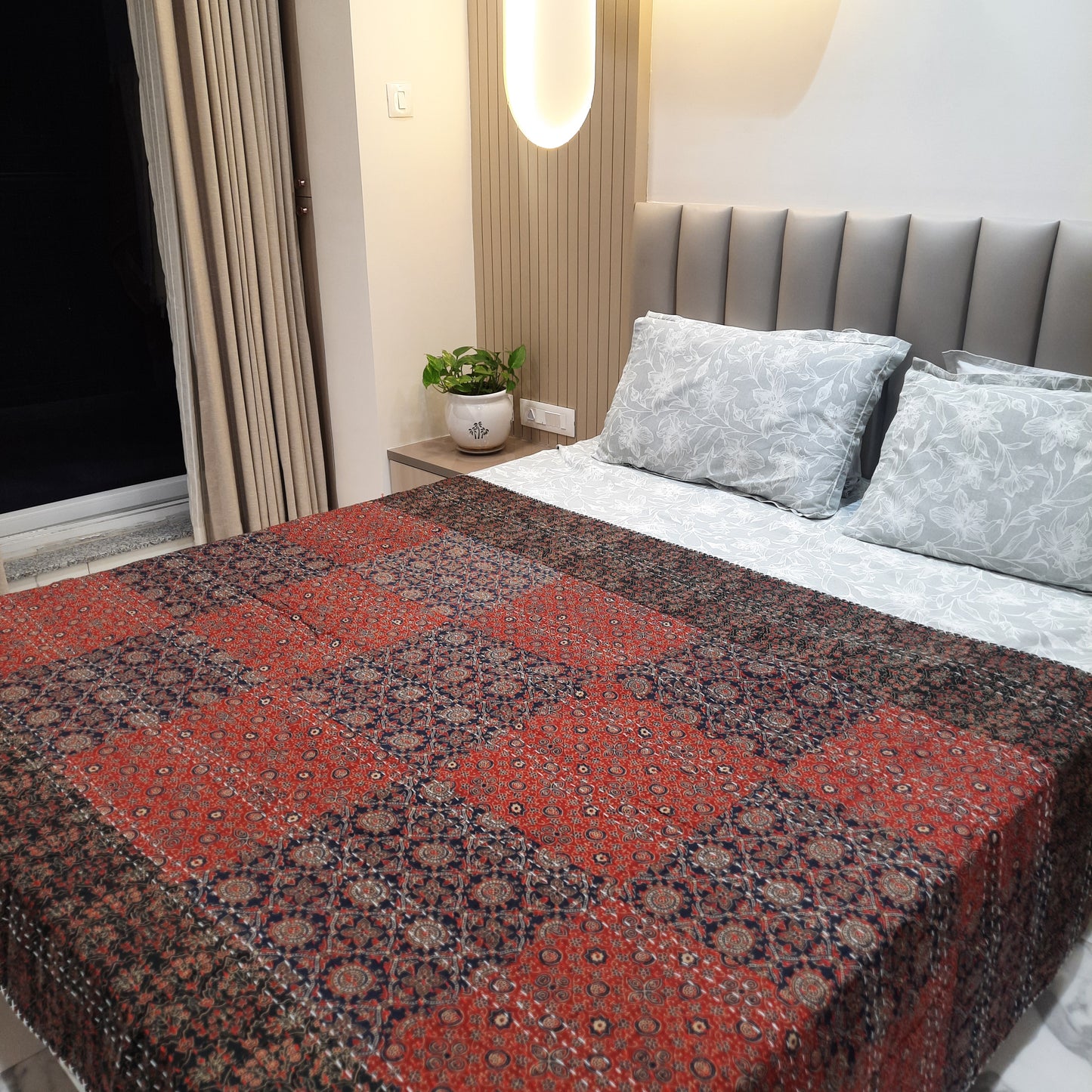 A multicolored geometric patterned bedcover displayed on a bed in a room setting with pillows and a headboard.