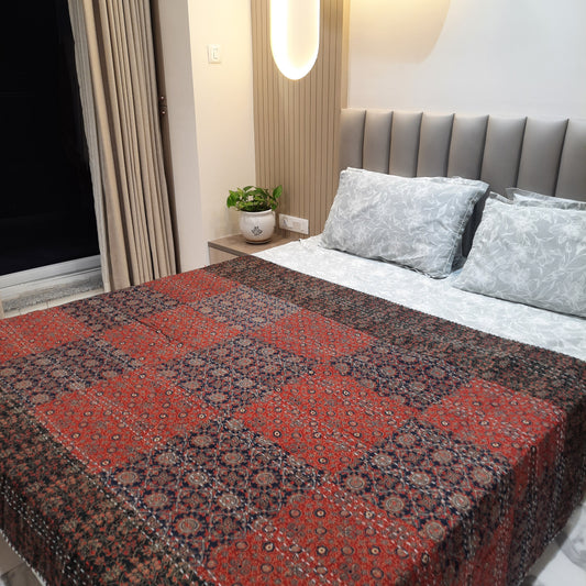 A multicolored geometric patterned bedcover displayed on a bed in a room setting with pillows and a headboard.