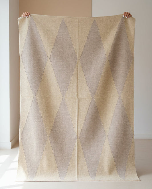 Beige and brown diamond patterned rug held by two hands against a neutral background