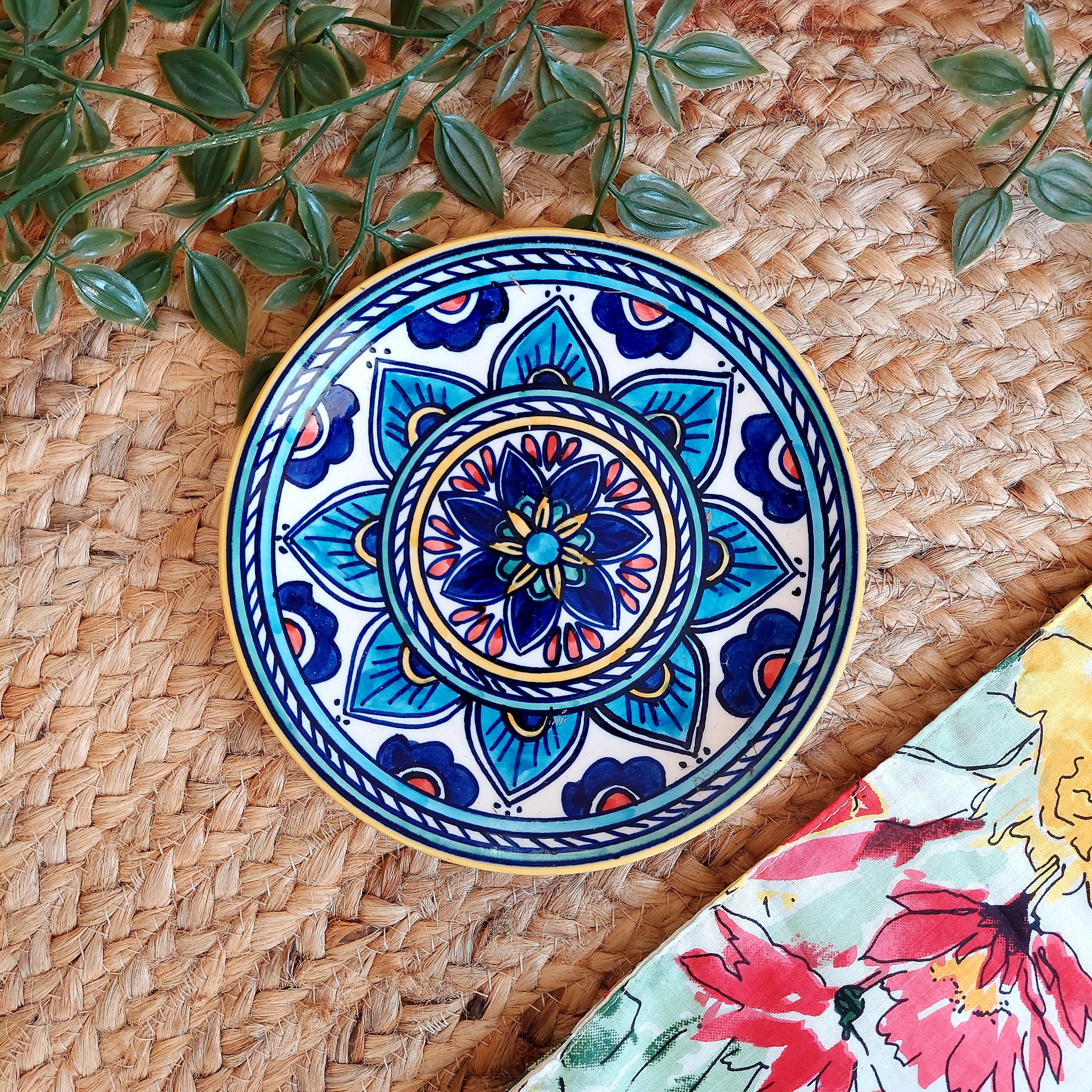 Decorative ceramic plate with blue floral design on a woven surface with leaves.