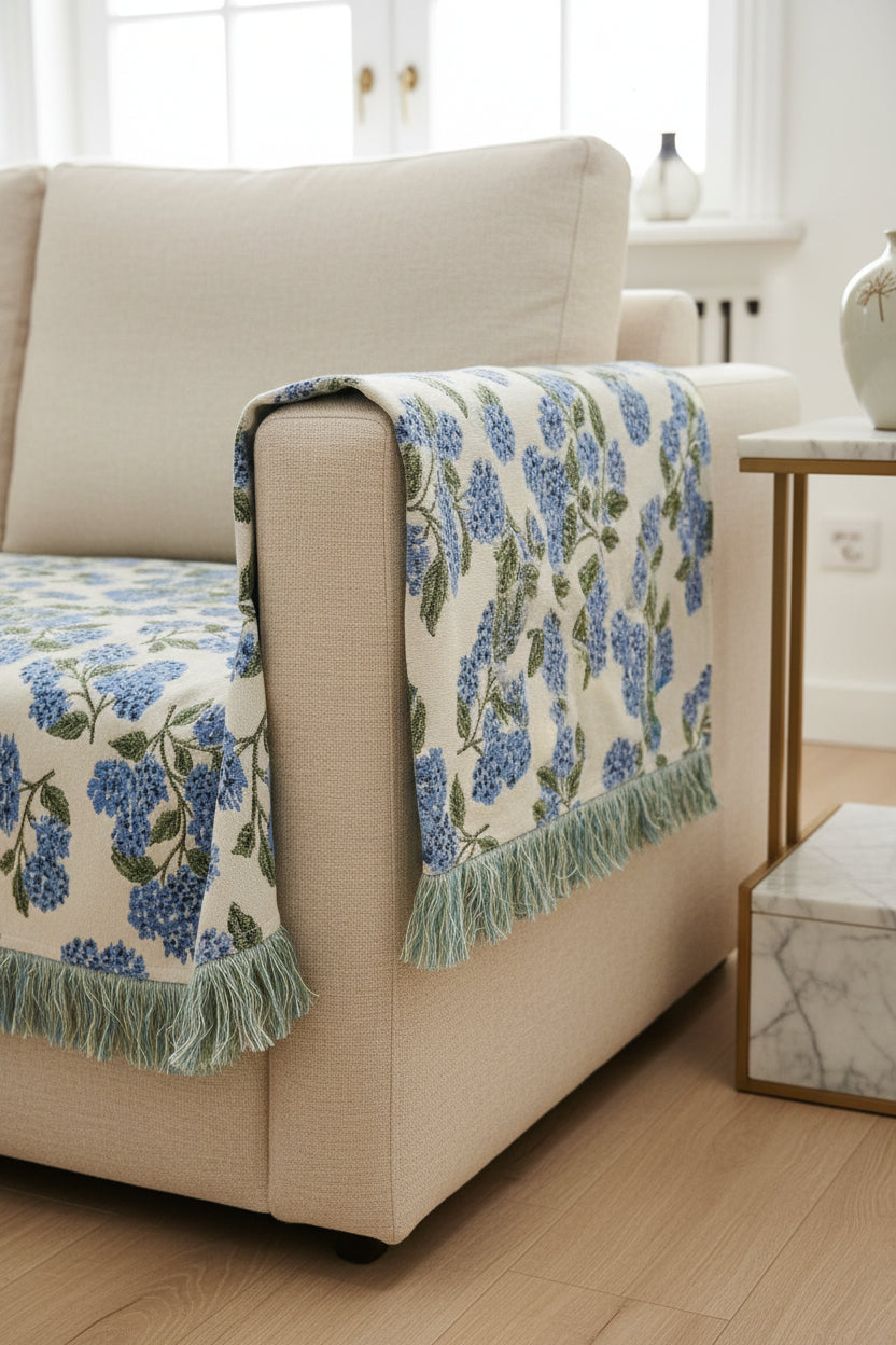 A close-up of a woven textile with a blue and green floral pattern on a white background, draped over a black chair with fringe along the bottom edge.