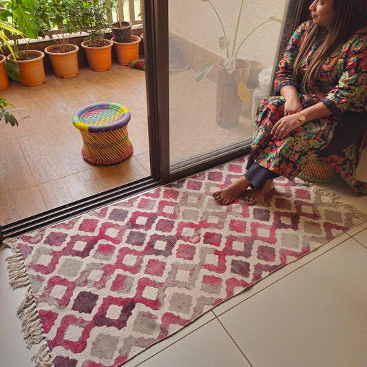 Boho-style cream base rug with pastel pink and grey shades and tassel edges, placed in a reading nook