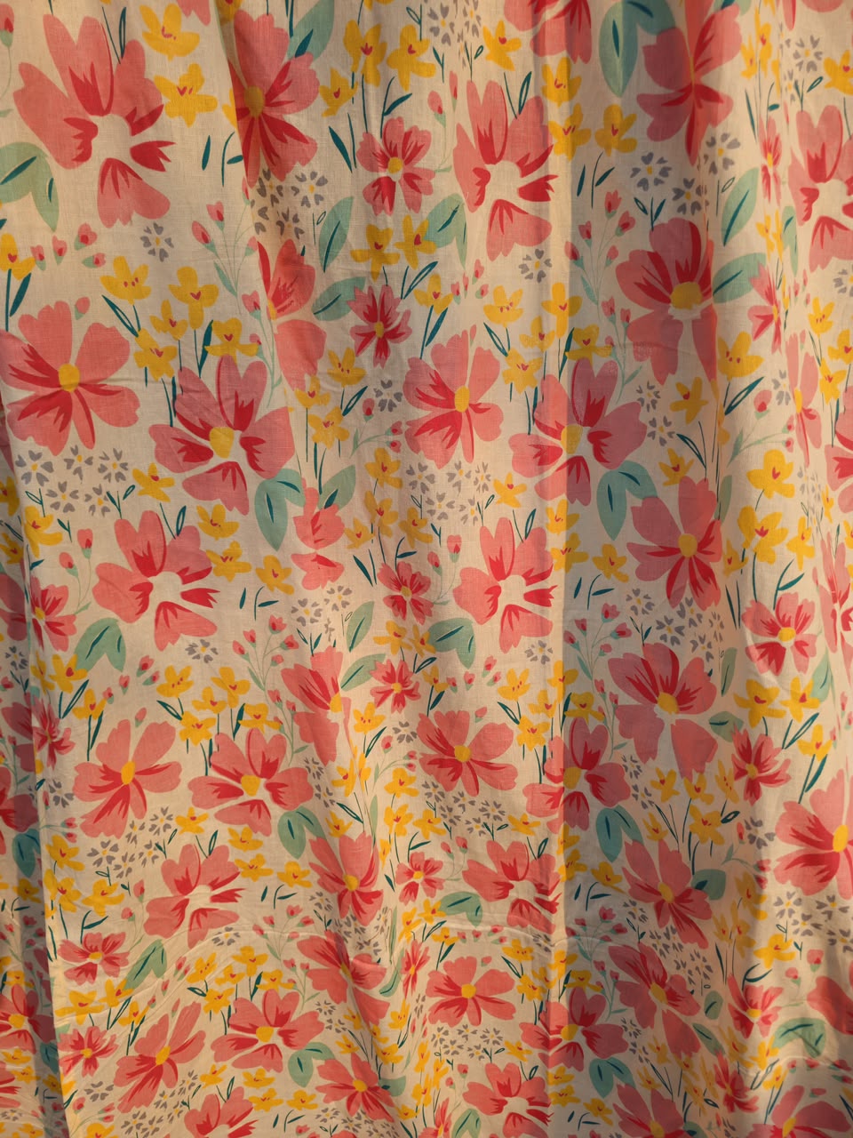 A close-up of a floral fabric with a repeating pattern of pink and yellow flowers, green leaves, and small gray dots on a light cream background.
