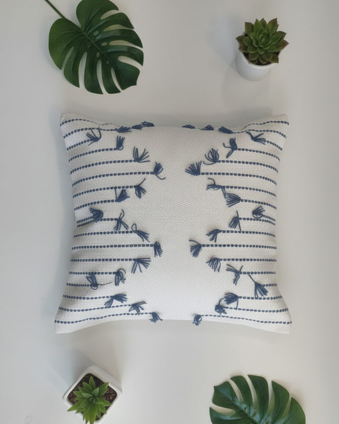 Decorative pillow with blue patterns on a white surface surrounded by small plants.