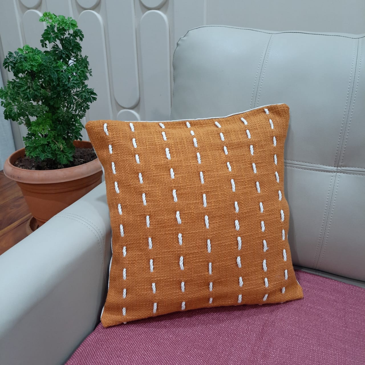 Detailed view of the hand-stitched threadwork on the rust orange cotton cushion cover.