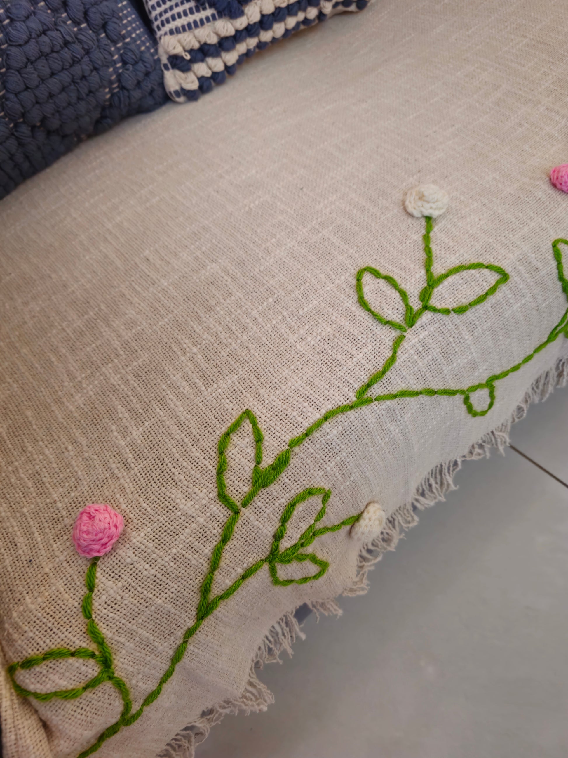 Embroidered fabric with green leaves and pink flowers on a beige background