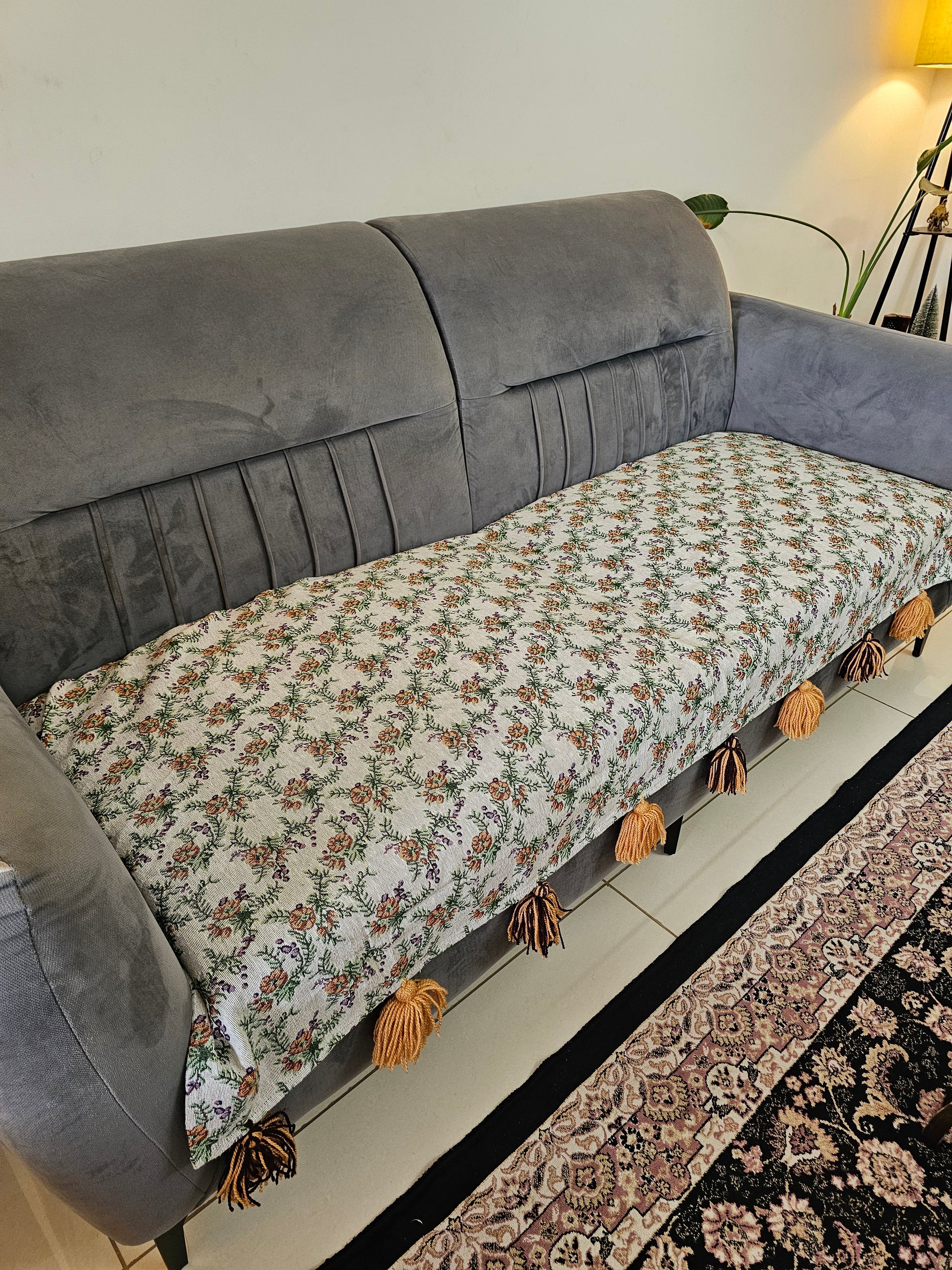 Floral-patterned fabric draped over a gray sofa with decorative tassels.