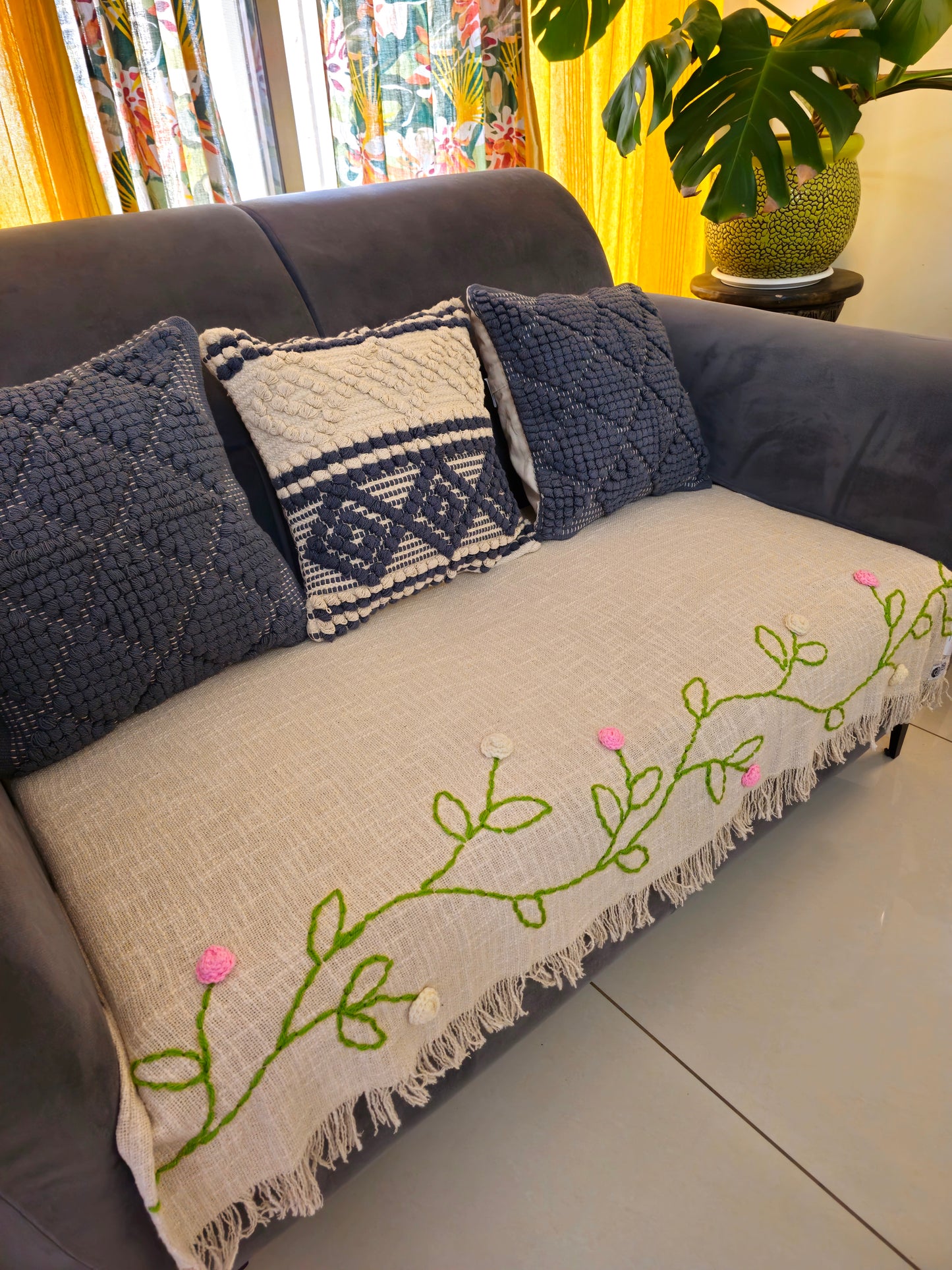 Gray sofa with decorative pillows and a blanket featuring floral embroidery.