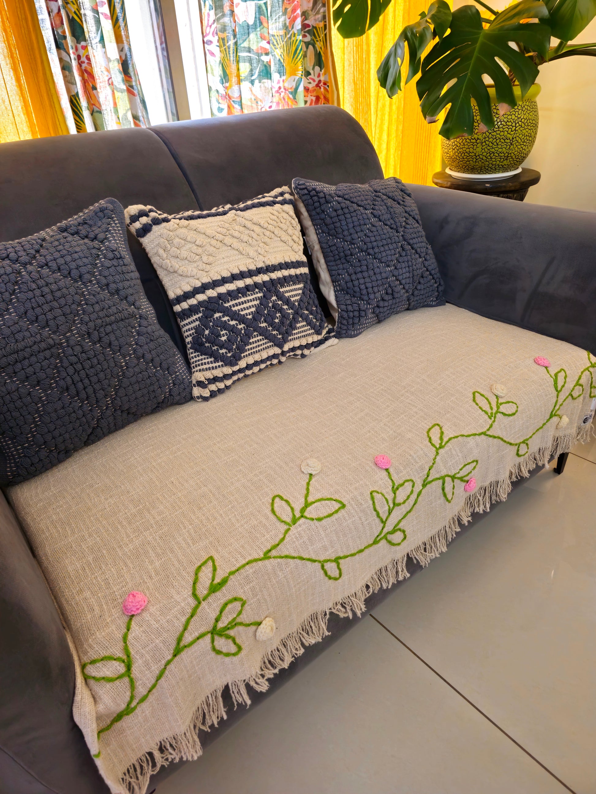 Gray sofa with decorative pillows and a blanket featuring floral embroidery.