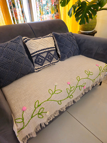 Gray sofa with decorative pillows and a blanket featuring floral embroidery.
