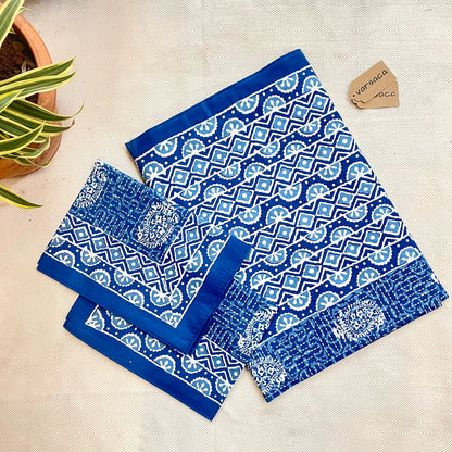 Folded indigo blue batik print king-size bedsheet with a plain border and geometric zigzag pattern on the border, displayed on a flat surface.