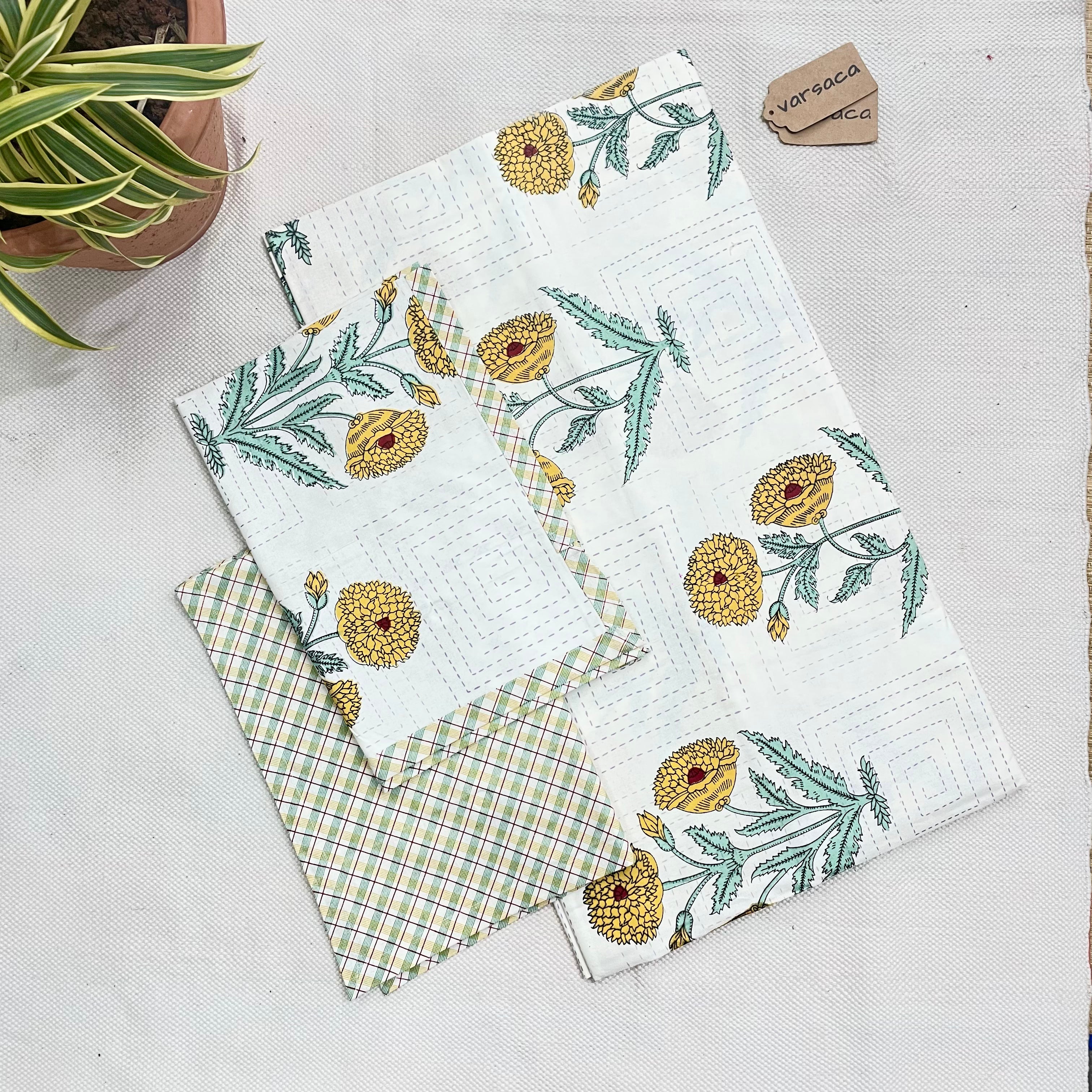 A king-size bedsheet with a yellow and white hand block print design, laid out flat with a part of the design showing a pineapple motif, placed on a white surface with a partial view of a green and white patterned fabric in the background.