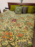 Floral patterned bedspread on a bed with green pillows and a book.
