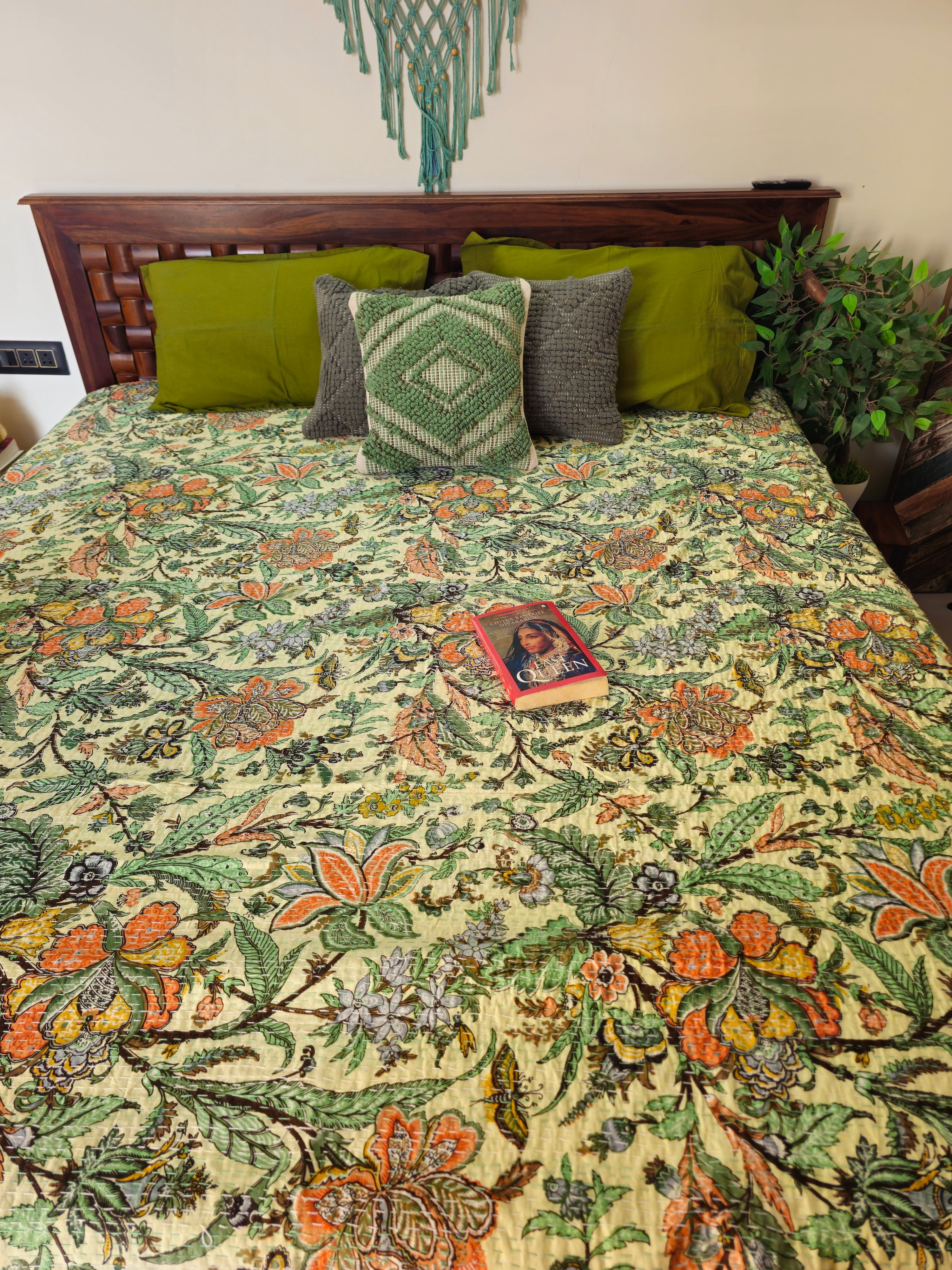 Floral patterned bedspread on a bed with decorative pillows and a plant in the background.