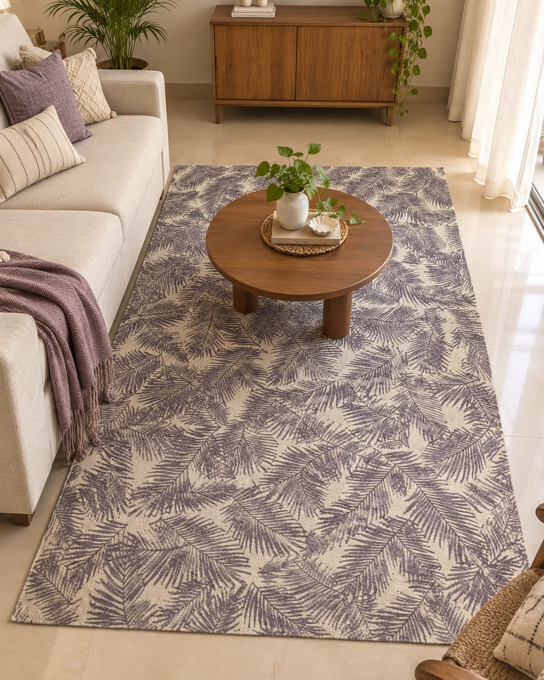 A full view of a muted purple and cream botanical leaf patterned flatweave cotton area rug styled in a modern living room with a light sofa and wooden coffee table.