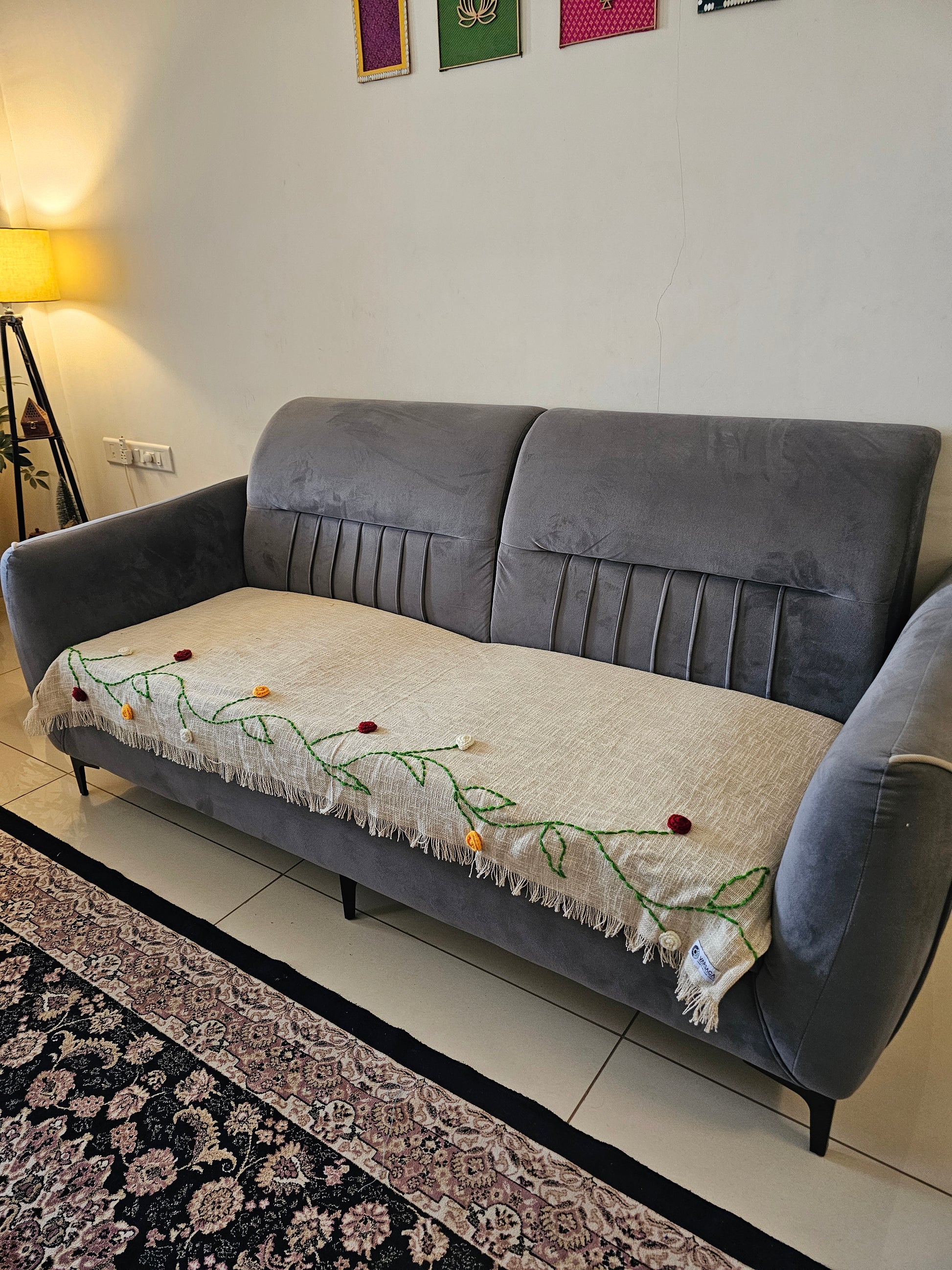 Gray sofa with a decorative blanket featuring floral patterns on a tiled floor.