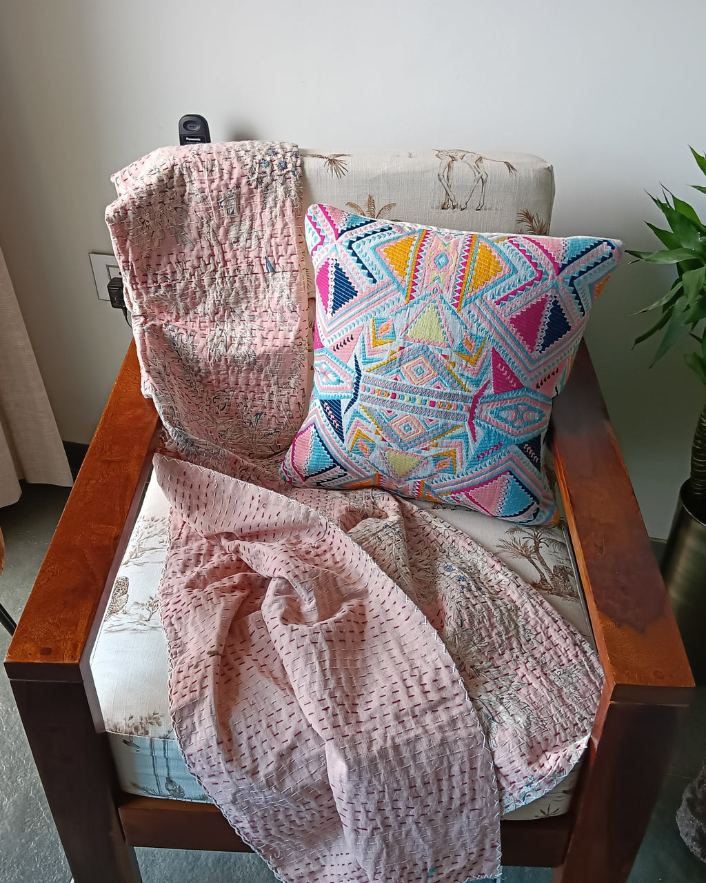 Chair with a pink blanket and colorful pillow, next to a wooden table with flowers and a plant.