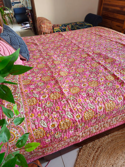 Pink floral quilt on a bed with a plant in the foreground