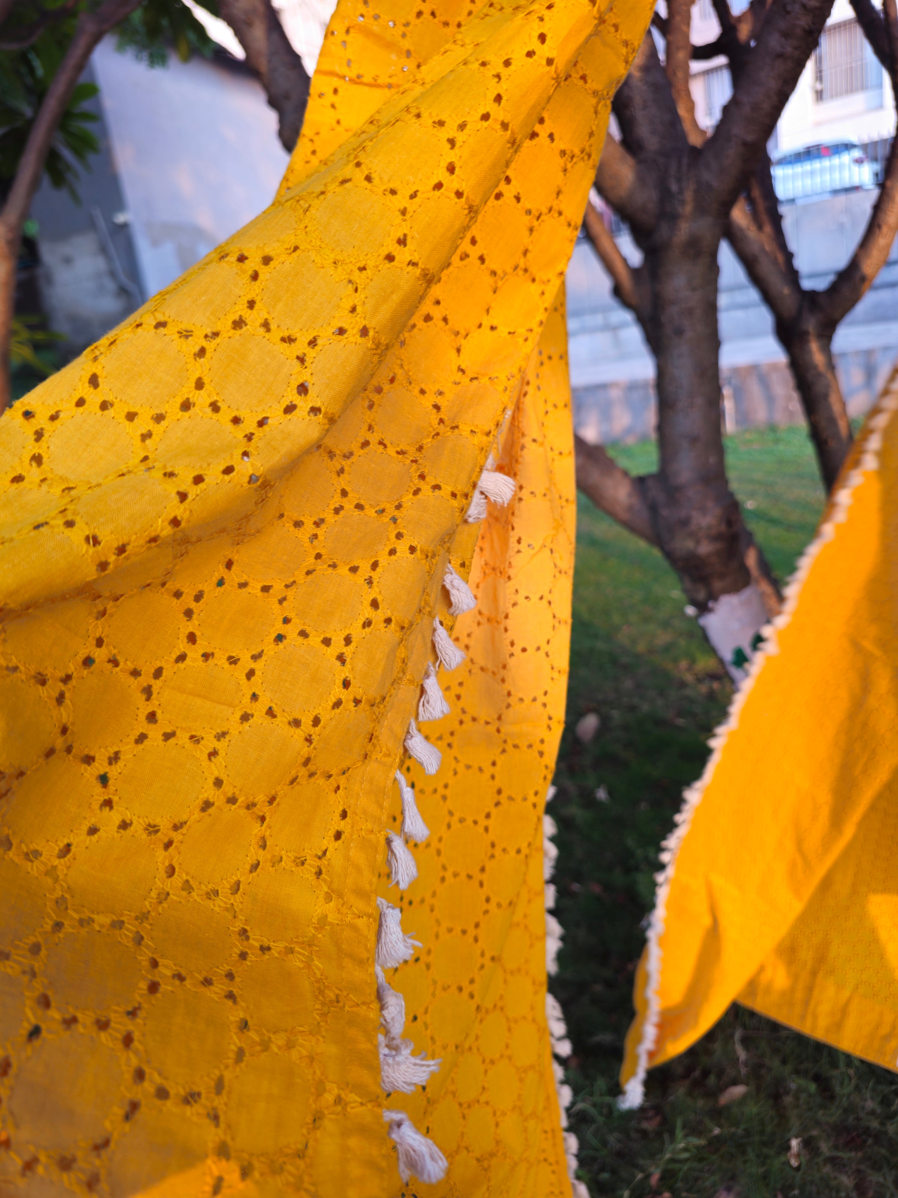 Close-up of a yellow fabric with a textured pattern, possibly a scarf or shawl, outdoors.