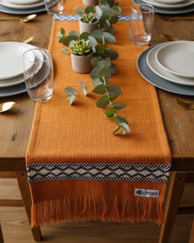 Dining table set with plates, glasses, and a decorative orange runner with a pattern.
