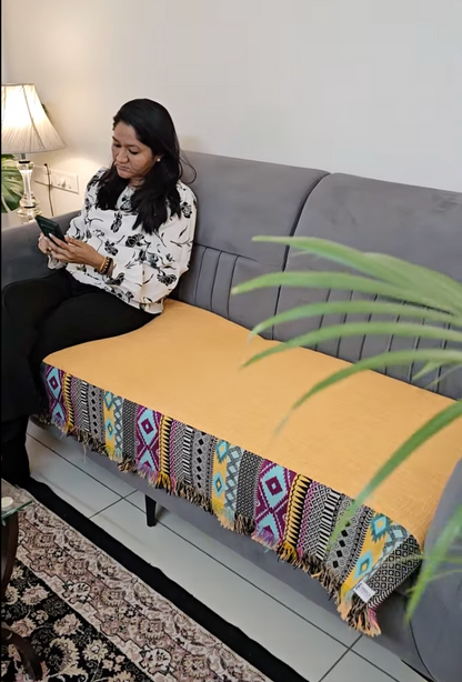 Woman sitting on a gray couch with a colorful patterned throw blanket