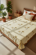 Bedroom with a bed covered in a floral quilt, surrounded by plants and a wooden nightstand.