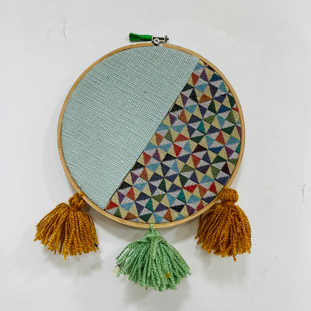 Embroidery hoop with geometric pattern and tassels on a white background